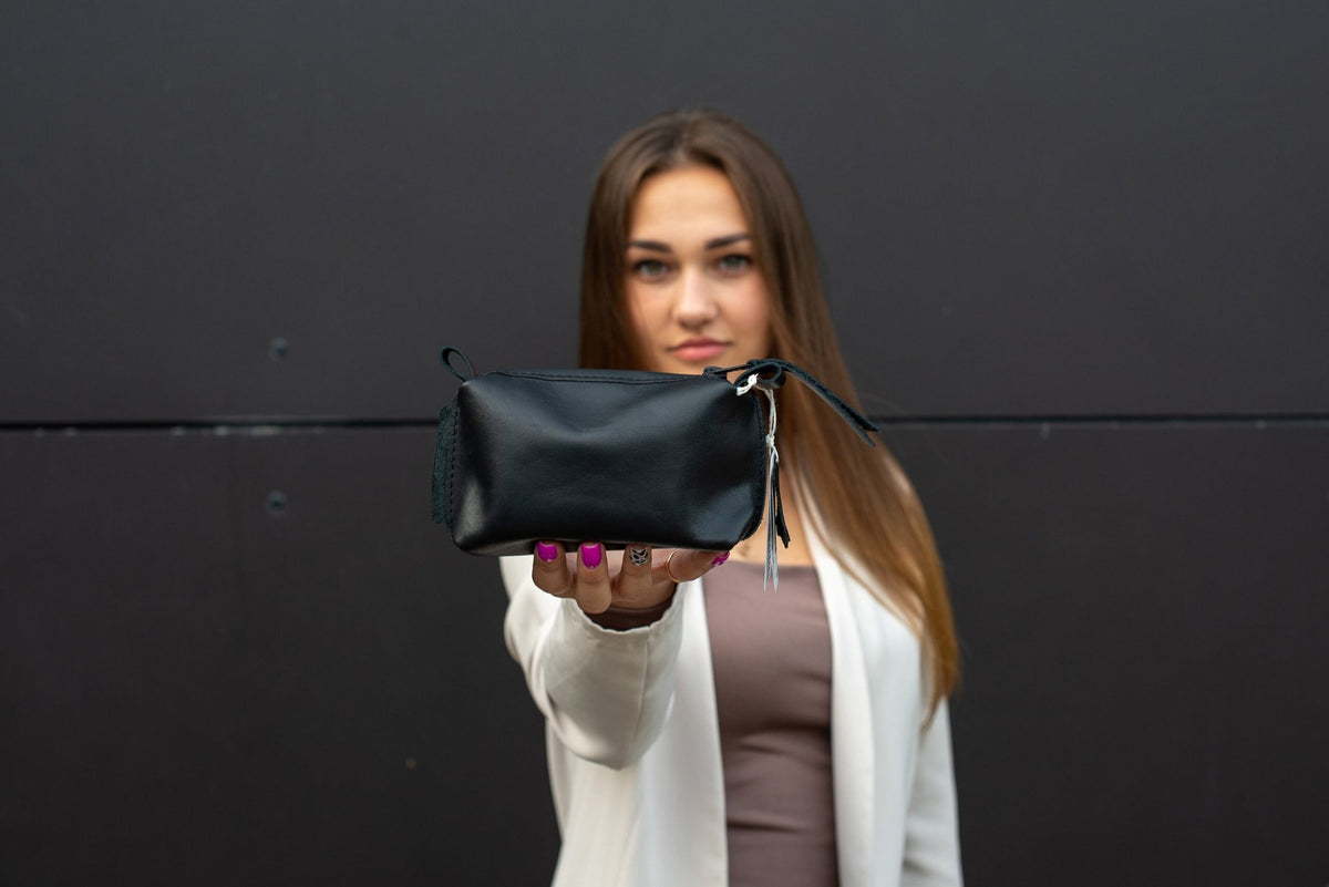 1. Woman holding Zelma Kraft black leather cosmetic bag, showcasing compact design and elegant style