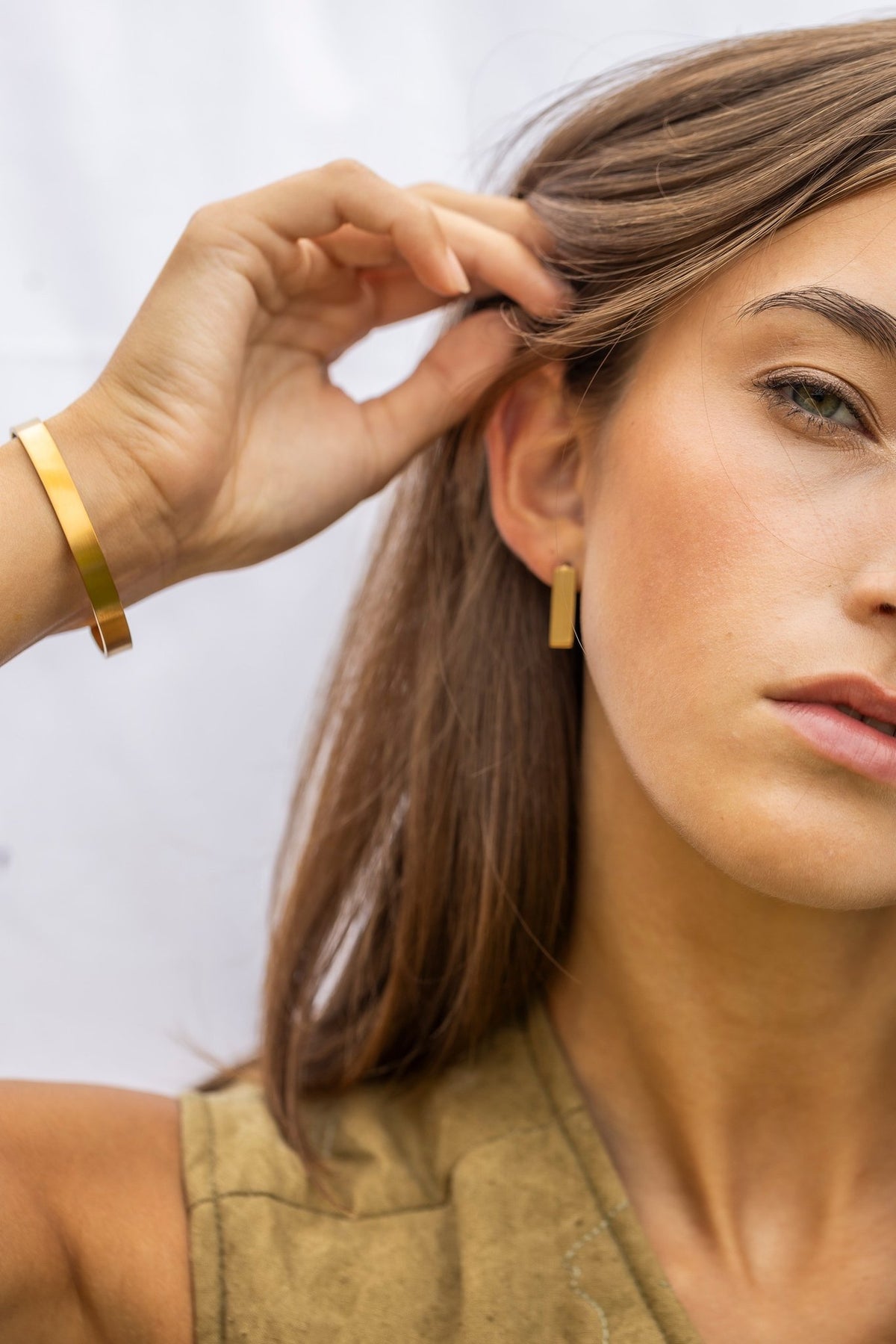 1. Woman adjusting hair while wearing Lentsius Sunlit earrings and bracelet against a light background