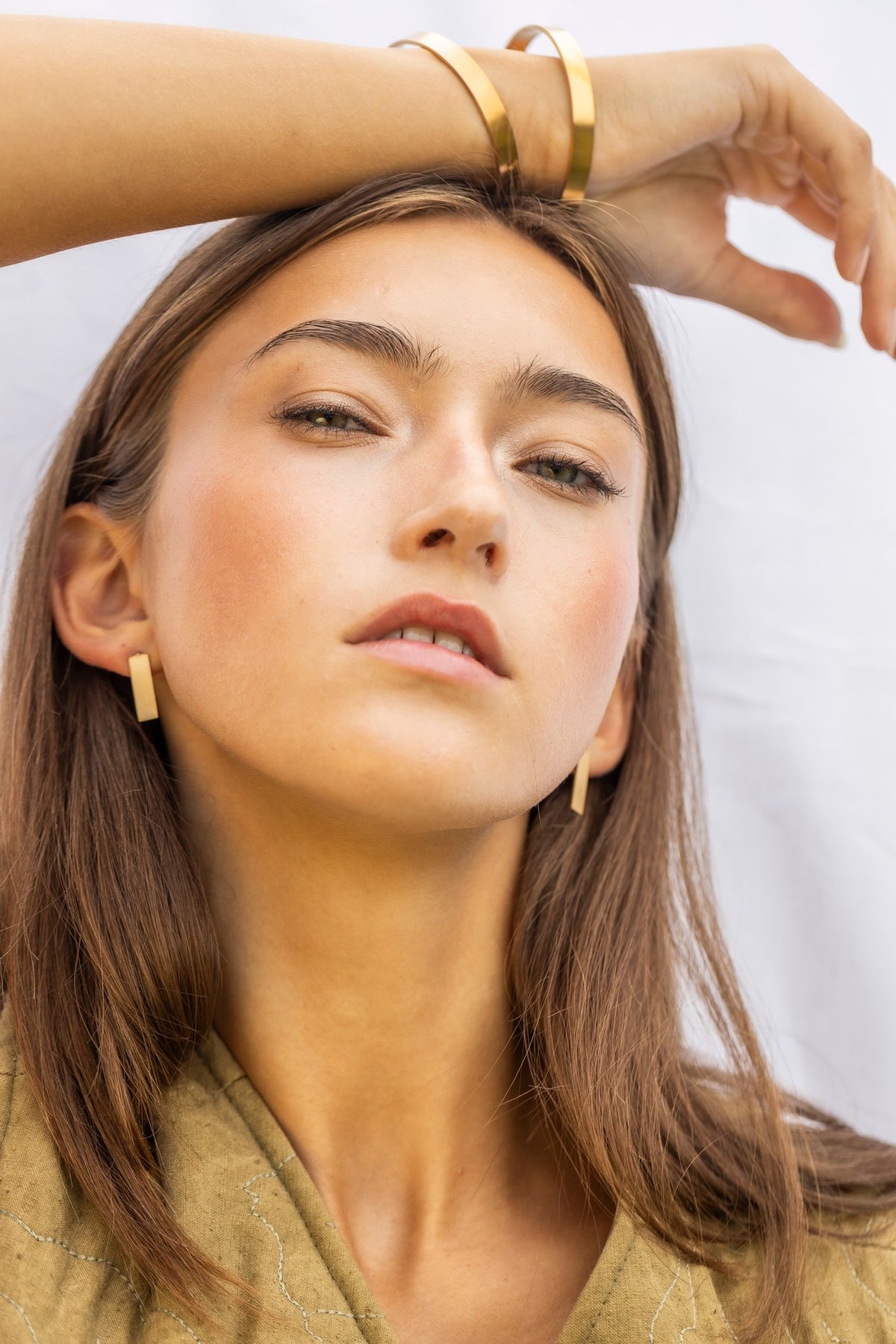 1. Woman wearing Lentsius Sunlit earrings and matching bracelet, posing with hand on head against a light background