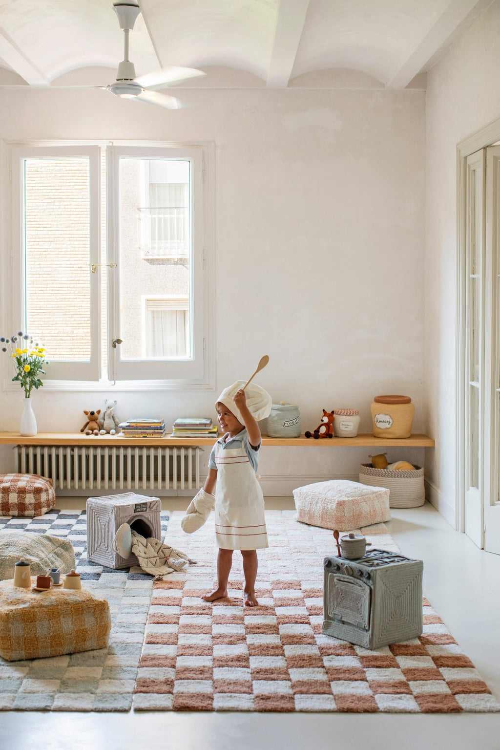 8. Child in chef outfit playing in bright room with Lorena Canals blue sage textile toy stove