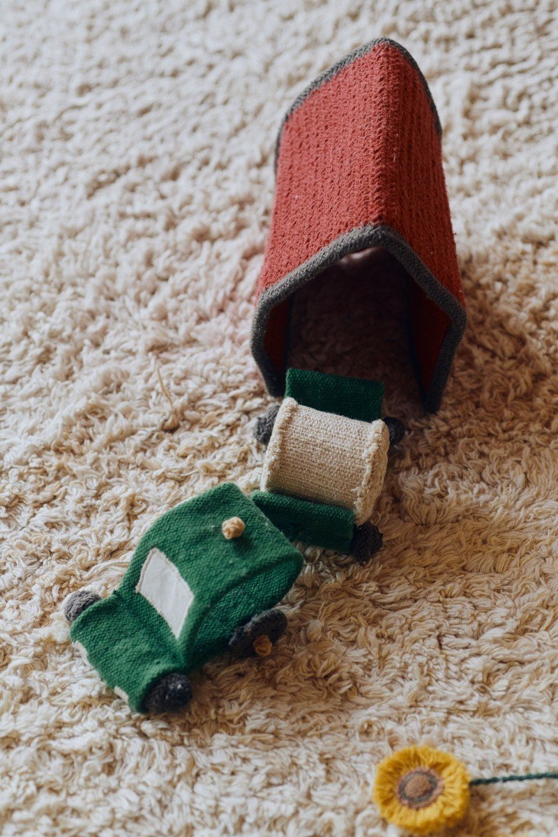 3. Close-up of Lorena Canals cotton play rug with mini tractor and stable toy on textured surface