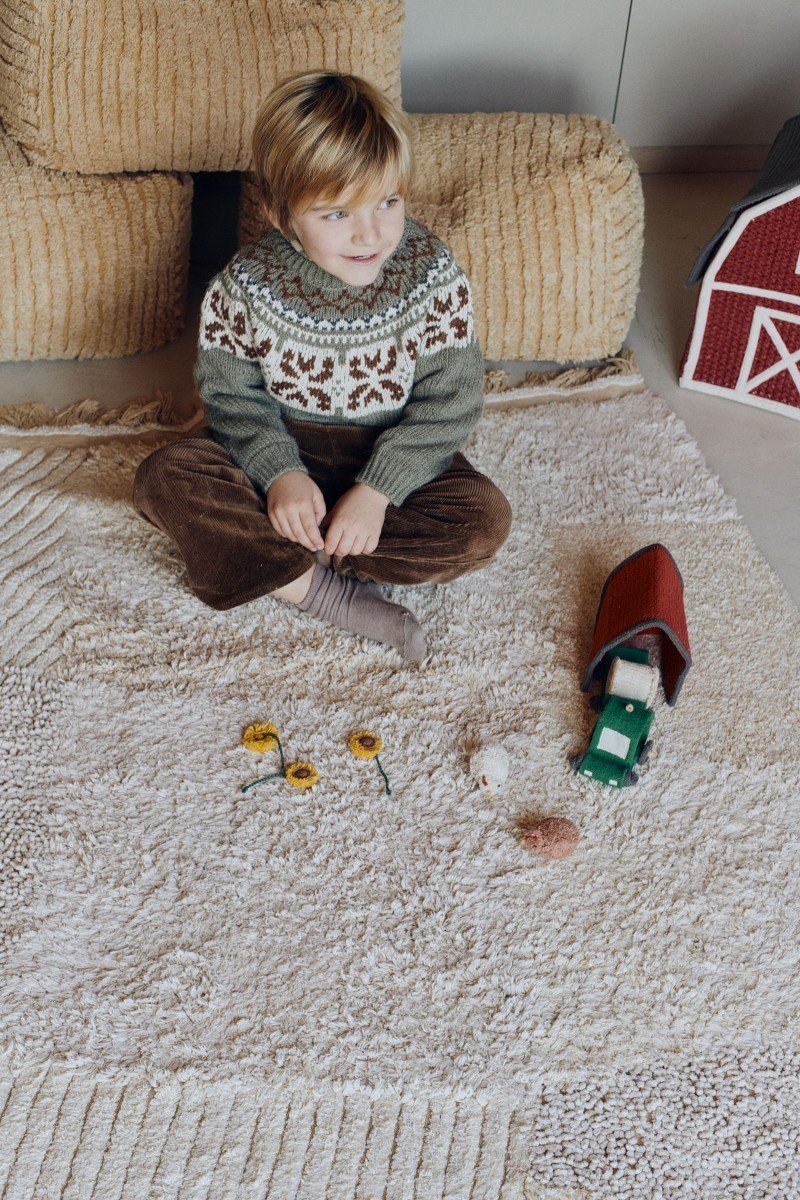 1. Child sitting on Lorena Canals cotton play rug with farm-themed toys, including a mini stable and tractor, in a cozy room setting