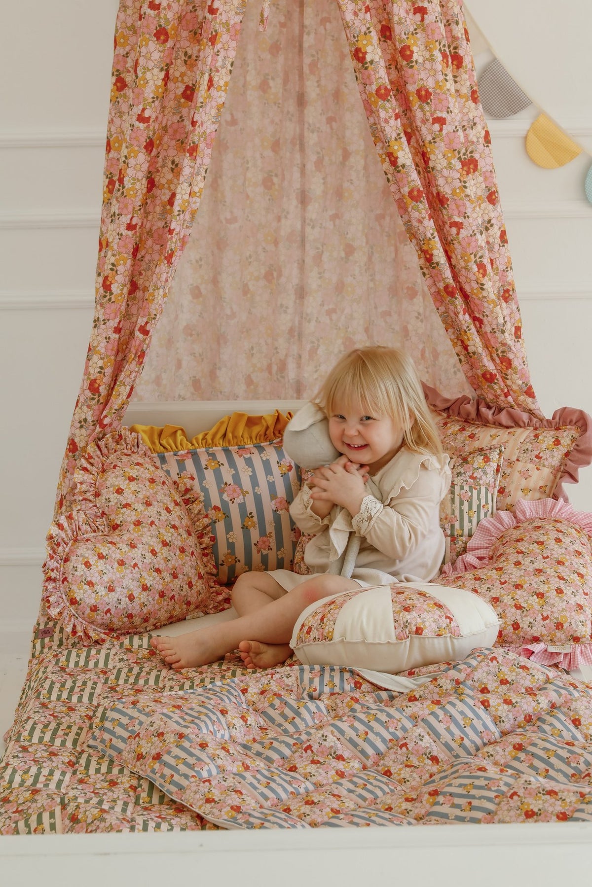 2. Child sitting on bed with Moi Mili cotton quilted patchwork blanket and pillow set in green garden pattern under floral canopy