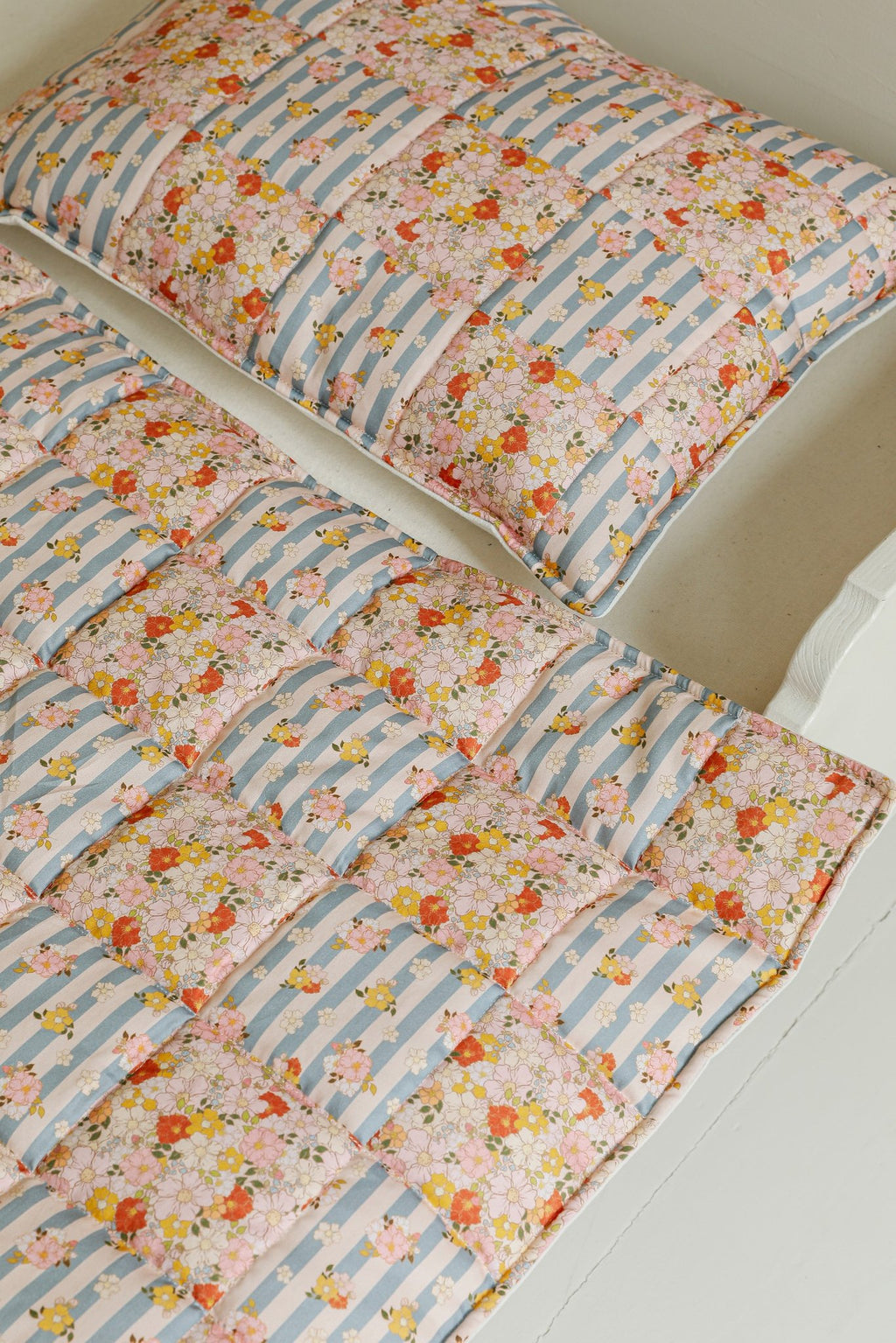 3. Detail of Moi Mili cotton quilted patchwork blanket and pillow on bed showing floral and striped design