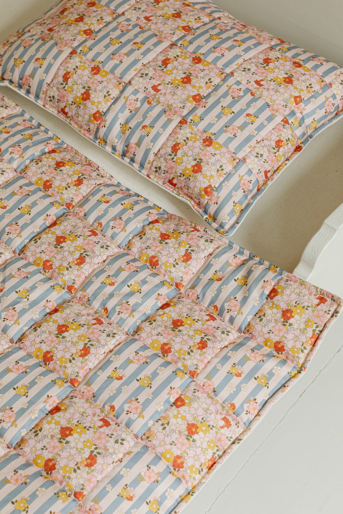 3. Detail of Moi Mili cotton quilted patchwork blanket and pillow on bed showing floral and striped design