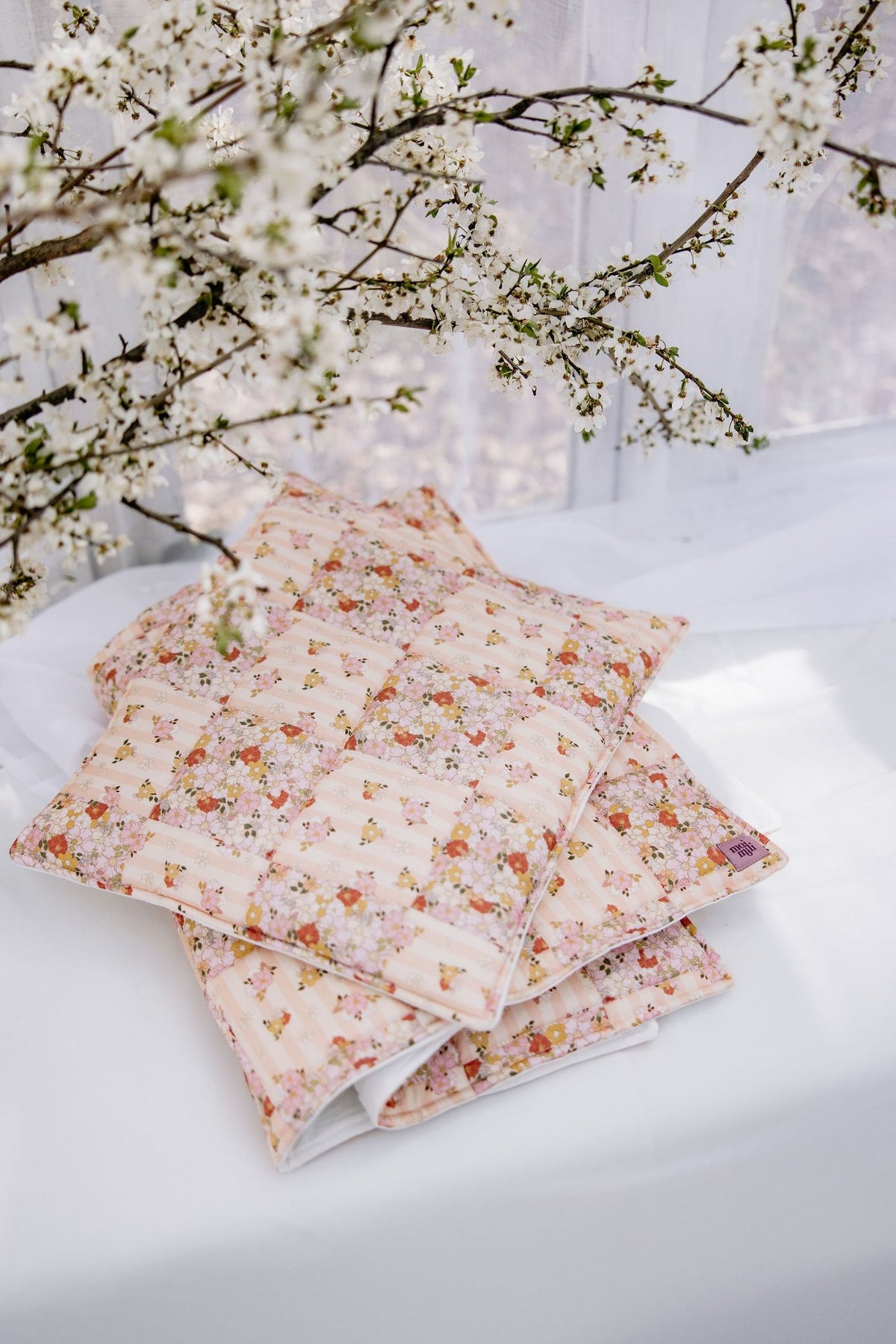 4. Floral cotton quilted blanket and pillow set folded on white surface with blooming branches
