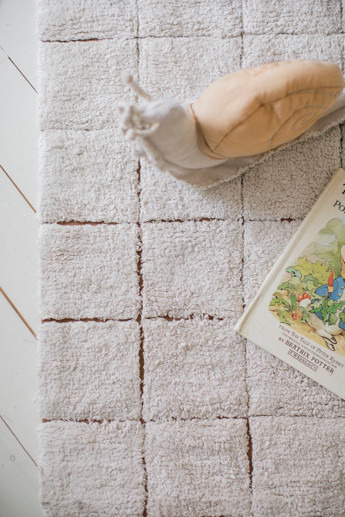 3. Close-up of Lorena Canals mosaic cotton rug showing toffee-colored grid pattern with book and cushion