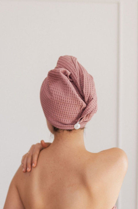 1. Woman with back turned wearing pink cotton waffle hair towel turban in indoor setting