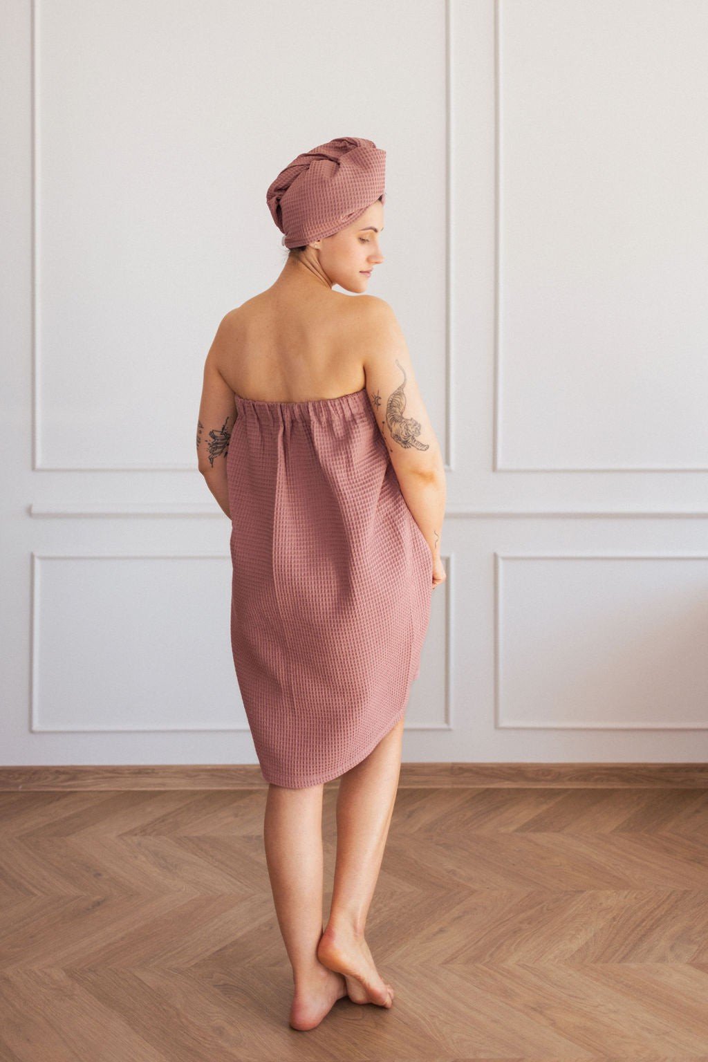1. Woman in old pink cotton waffle sauna wrap with matching head wrap, shown from back in room with wooden floor