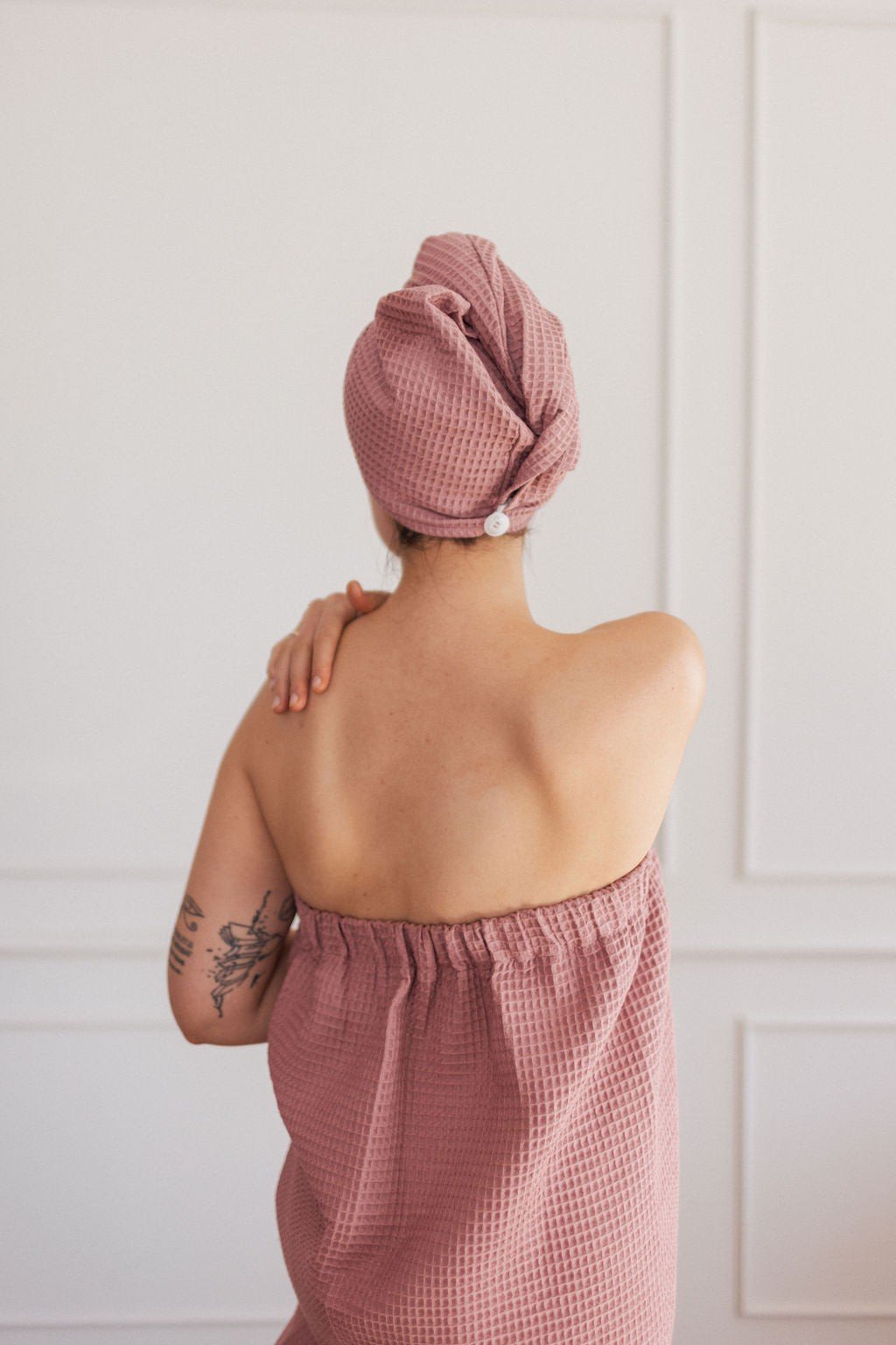 1. Woman in old pink cotton waffle sauna wrap with matching head wrap, shown from back in room with white walls