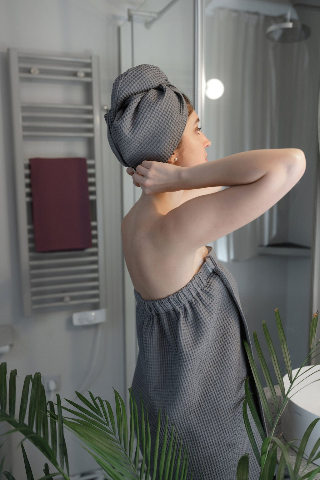 1. Woman in gray cotton waffle sauna wrap with matching head wrap, adjusting hair in bathroom setting