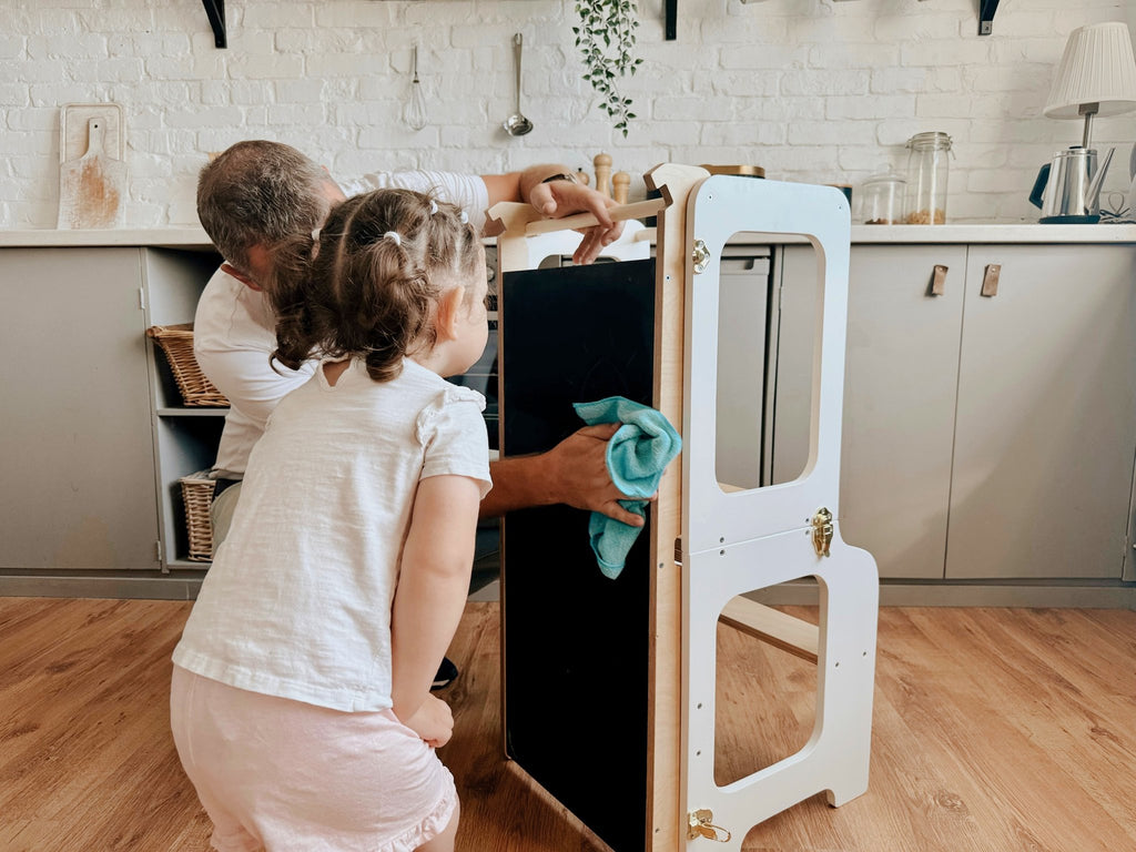2. Child and adult cleaning a blackboard on a white learning tower in a kitchen