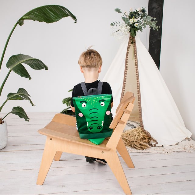 7. Boy sitting with Muni crocodile backpack in indoor setting with teepee