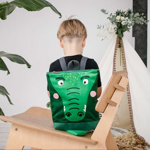 9. Boy wearing Muni crocodile backpack sitting on chair in studio