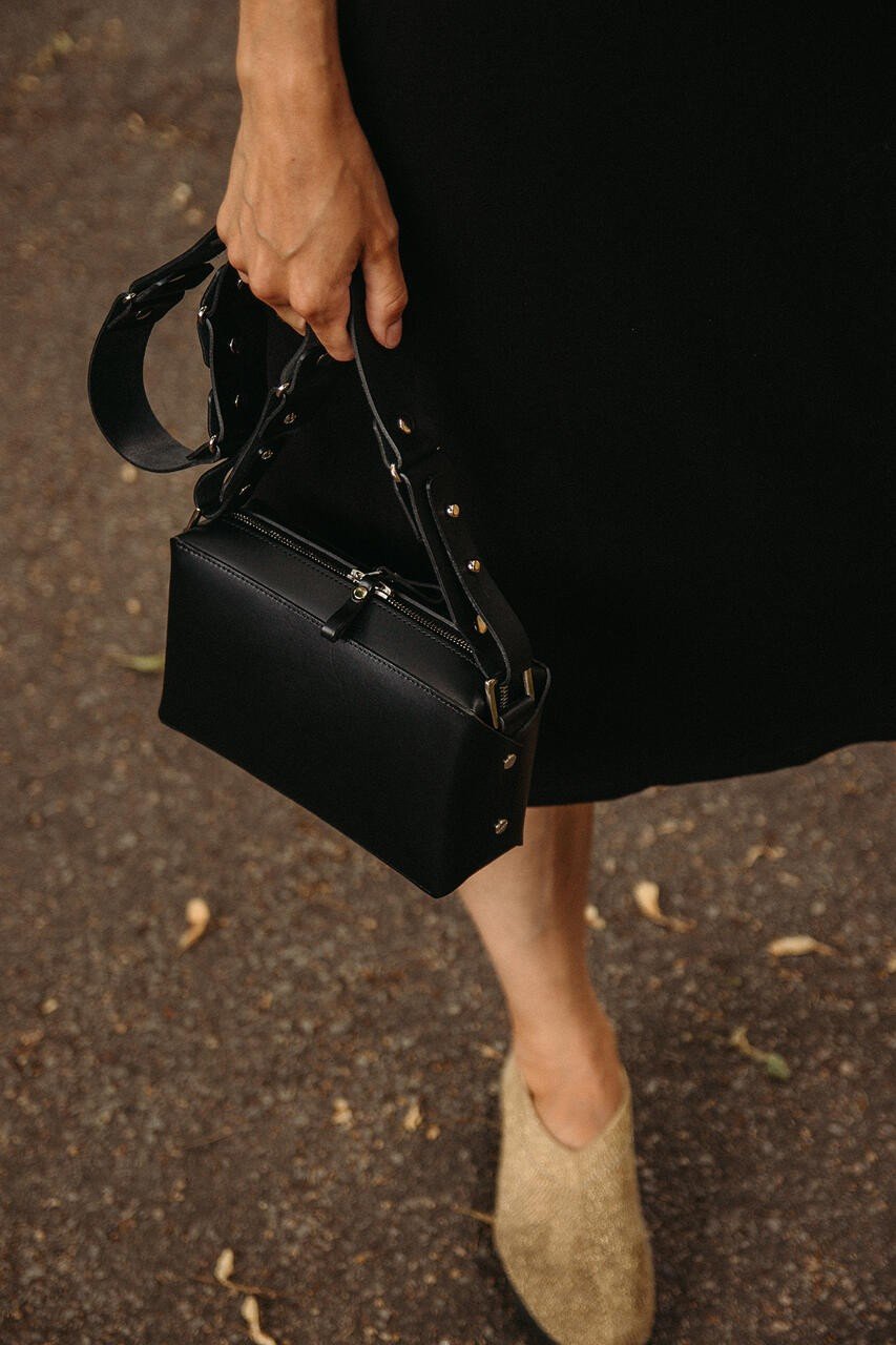 1. Woman holding Stella Soomlais black crossbody bag with adjustable strap on urban street