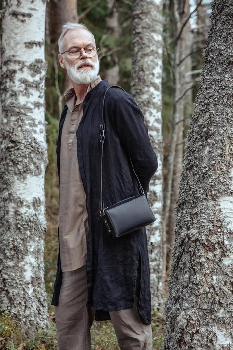 1. Man wearing black long coat with Stella Soomlais black crossbody bag in forest setting