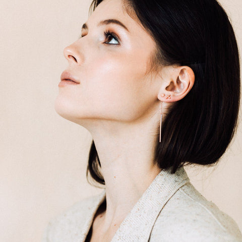 1. Woman wearing rose gold Crux earrings with short dark hair, looking upwards