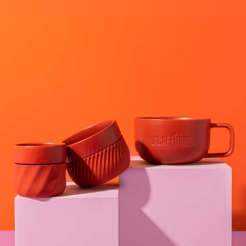 1. La Cafetière red coffee mugs set of three on pink blocks with orange background, showcasing different sizes and silicone bands