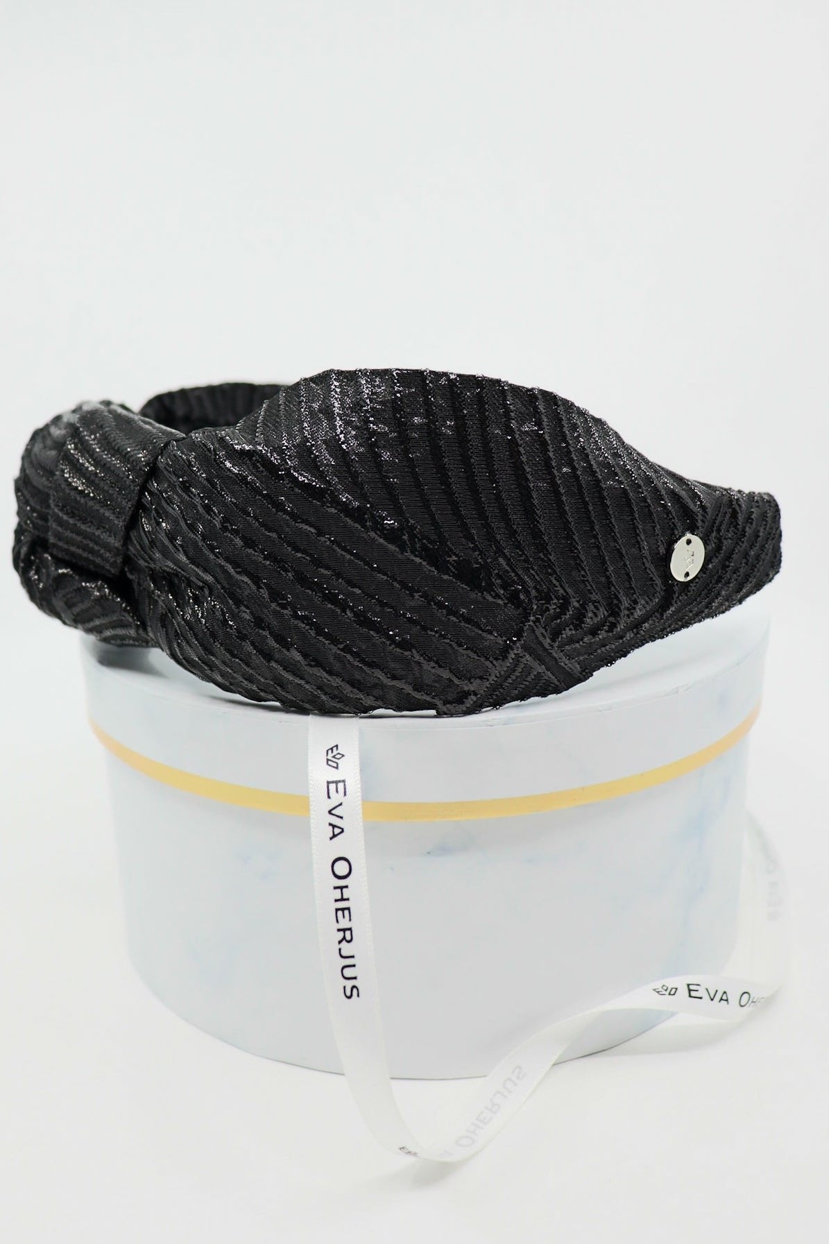 4. Close-up of Eva Oherjus Knot Headband Holly in black with metallic threads, displayed on a luxury hat box