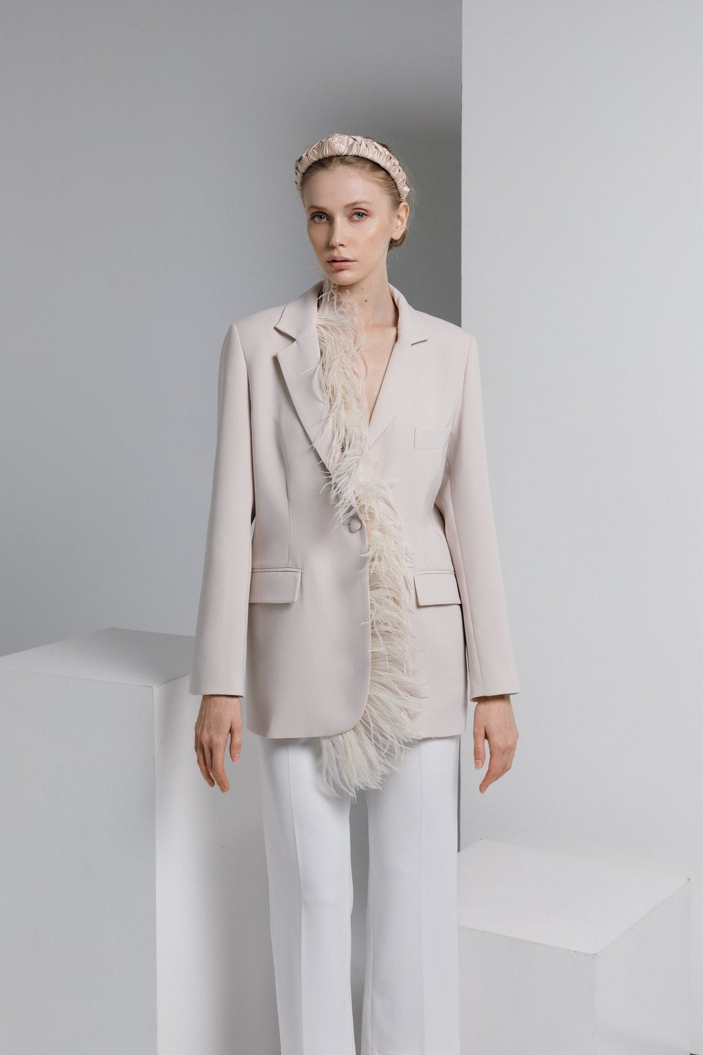 1. Woman wearing Eva Oherjus Jenna Mulberry Silk Knotted Headband in light beige, styled with a chic blazer in a studio setting