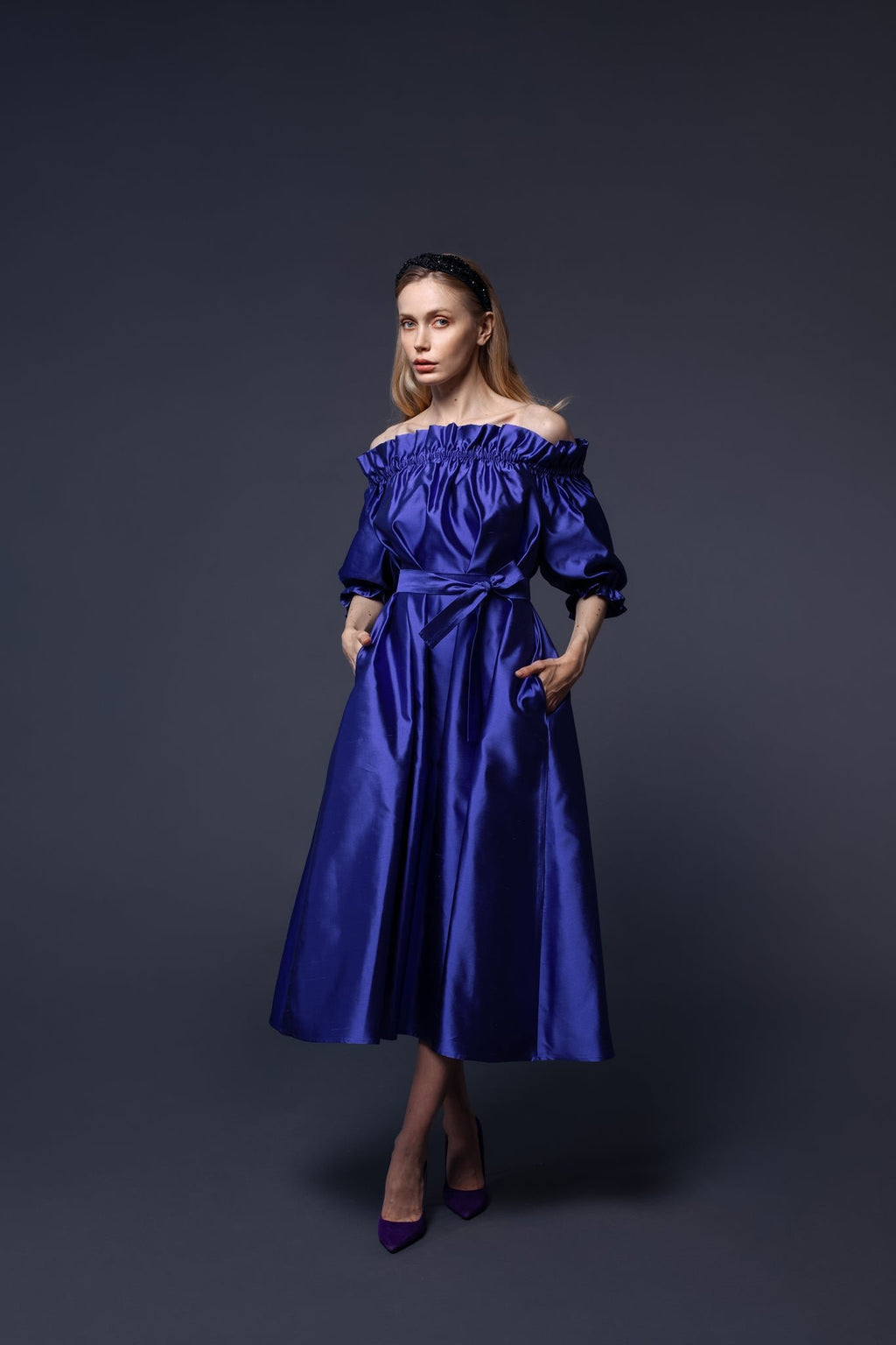 1. Woman wearing Eva Oherjus Mulberry Silk Beaded Headband Hestia with black shiny beads, styled with an elegant blue dress in a studio setting