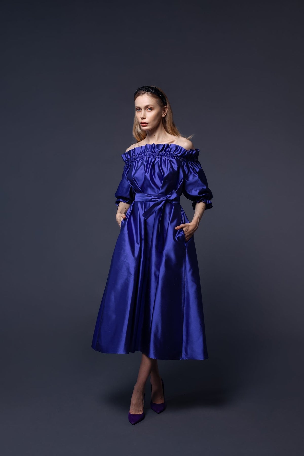 1. Woman wearing Eva Oherjus Mulberry Silk Beaded Headband Hestia with black shiny beads, styled with an elegant blue dress in a studio setting