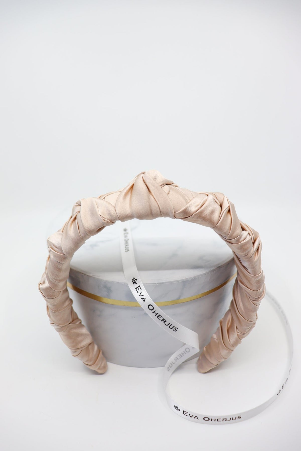 4. Front view of Eva Oherjus Jenna Mulberry Silk Knotted Headband in light beige, highlighting knotted design on hat box