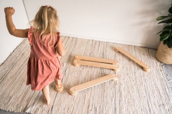 4. Child in pink dress walking on Ewart Woods wooden balance beams on a rug