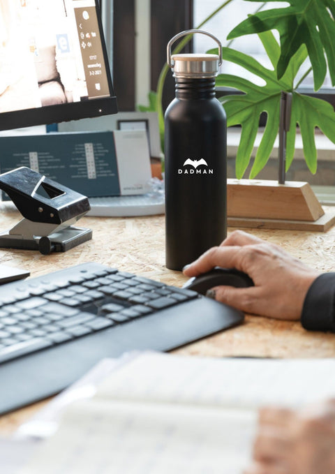3. Black DADMAN thermos bottle with bamboo lid on a desk beside a computer and plant