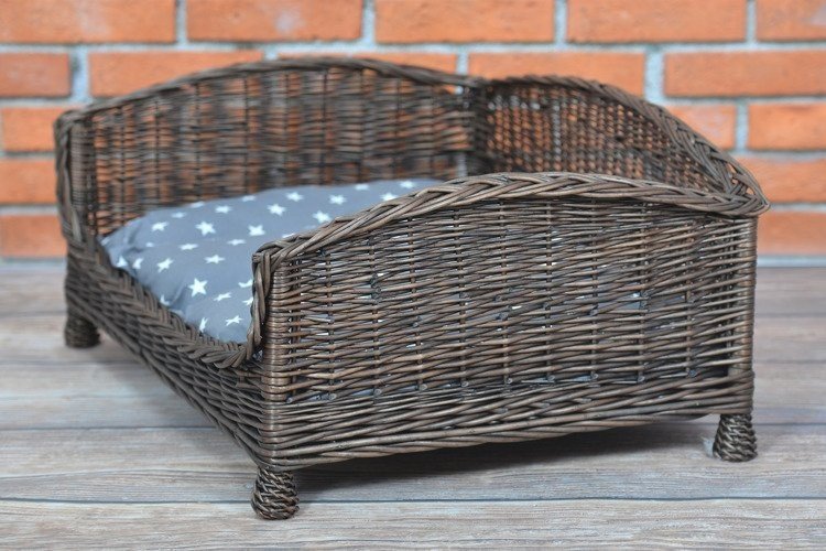 3. Side view of dark wicker pet bed with grey star-patterned cushion against brick wall