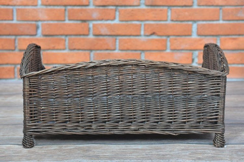 4. Back view of dark wicker pet bed against brick wall, showing woven design