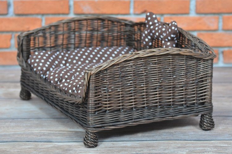 5. Side view of dark wicker pet bed with brown polka dot cushion and bone against brick wall