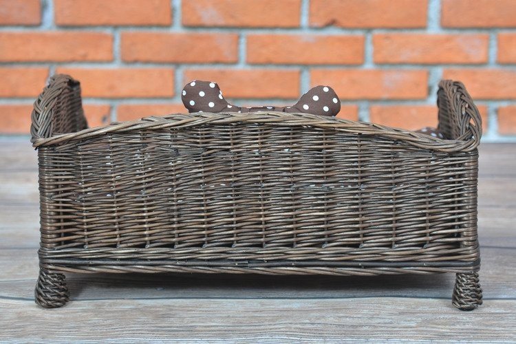 3. Back view of dark wicker pet bed with brown polka dot cushion and bone against brick wall