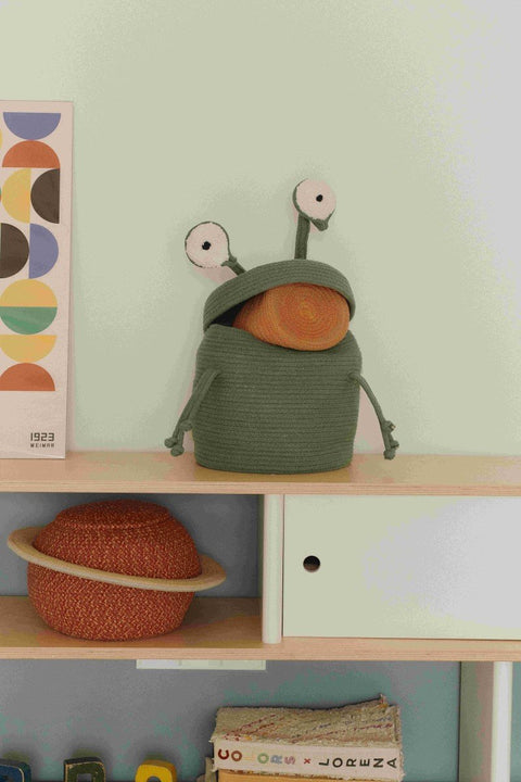 2. Green alien basket with lid open, revealing orange interior, placed on a shelf with other decorative items