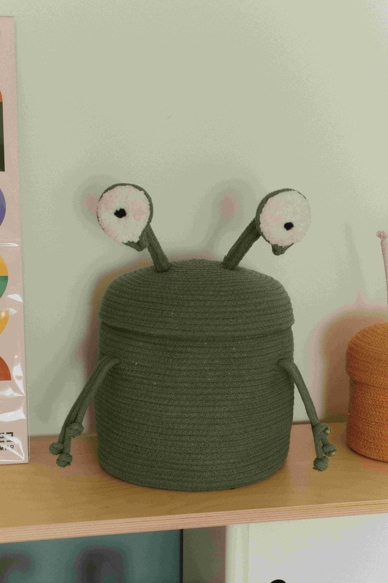 2. Green alien-themed basket with large white eyes and arm-like strings, placed on a shelf in a room setting