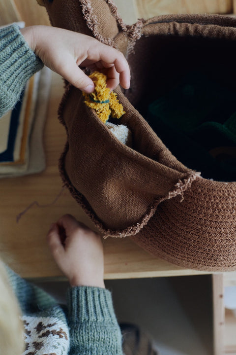 3. Child placing toys inside Lorena Canals chicken pouf, highlighting its practical use in a child's room