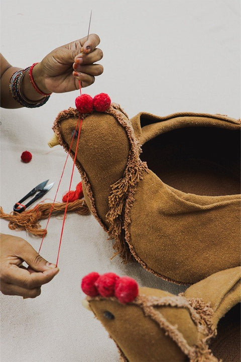 5. Detail of hand-sewing red pom-poms on Lorena Canals chicken pouf, emphasizing craftsmanship and quality