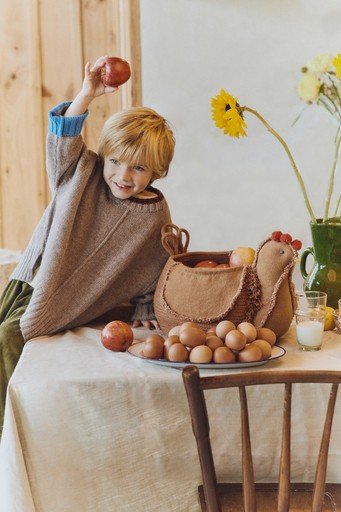 1. Child playing with Lorena Canals decorative chicken pouf on a table with eggs and flowers, creating a cozy, rustic atmosphere