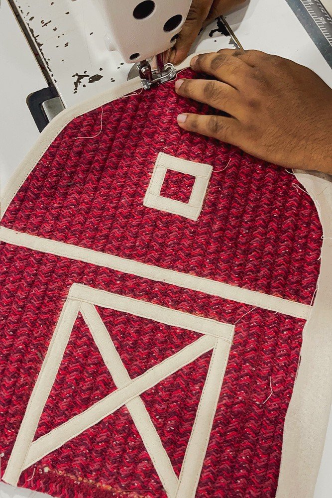 4. Close-up of hands sewing red barn-shaped decorative basket with white window and door details