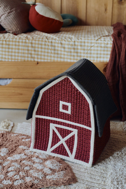 5. Red barn-shaped decorative basket with white window and door details placed in a rustic bedroom setting