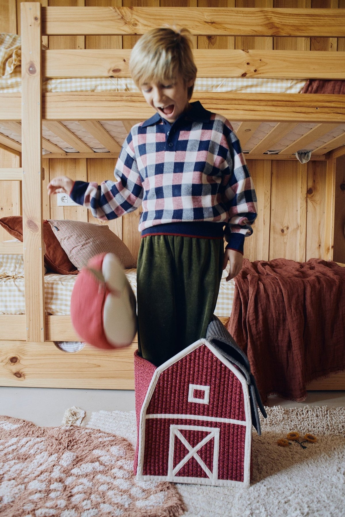 2. Boy playing with a red barn-shaped decorative basket featuring white window and door details in a rustic bedroom