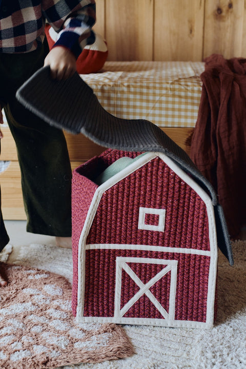1. Child opening the roof of a red barn-shaped decorative basket with white window and door details in a cozy room setting