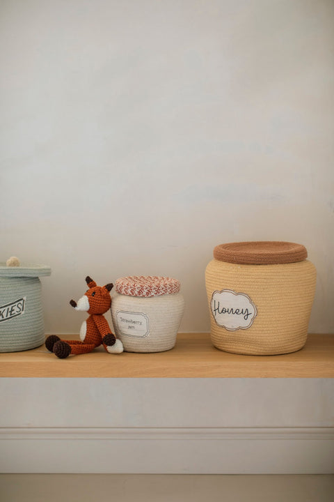 4. Decorative honey yellow basket with toffee brown lid labeled 'Honey' on wooden shelf next to toys
