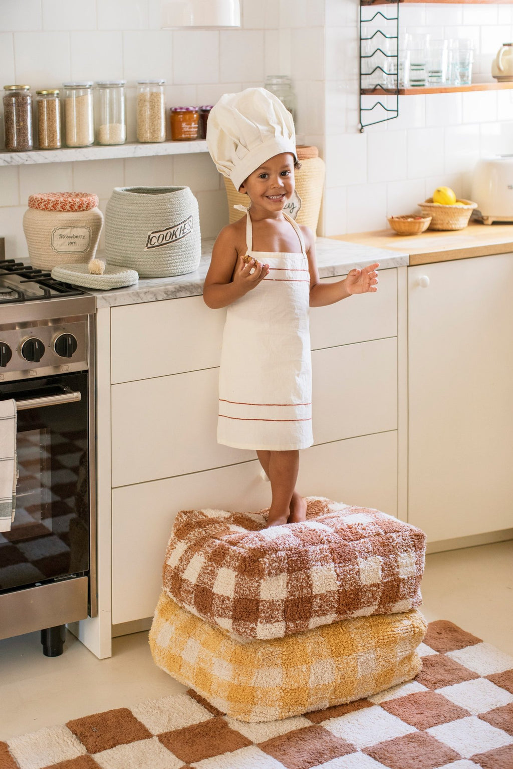 1. Child in kitchen with chef hat, standing near decorative baskets, including one with 'Strawberry Jam' label, highlighting playful decor