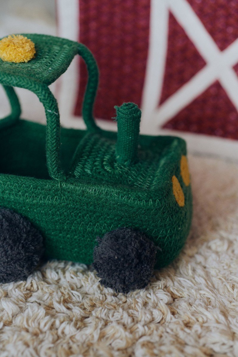 3. Close-up of green cotton tractor basket with yellow lights and black pompom wheels on textured carpet