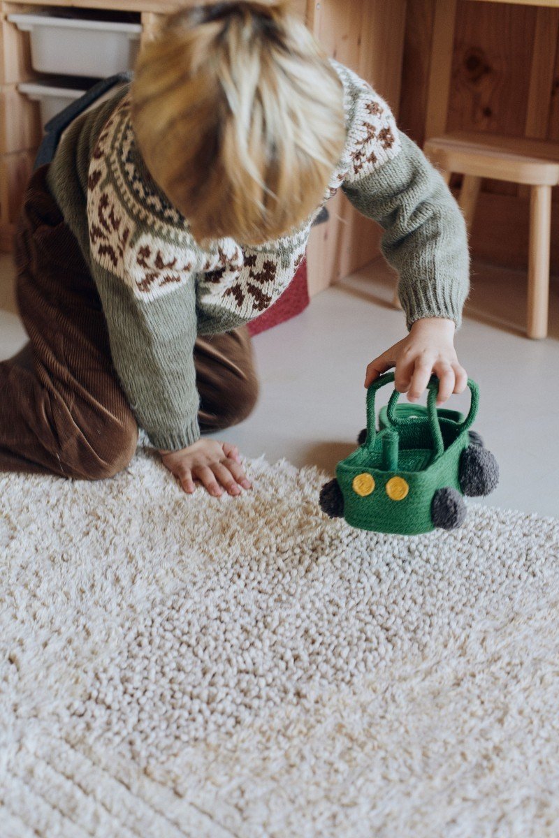 1. Child interacting with green tractor-shaped basket on a soft beige carpet