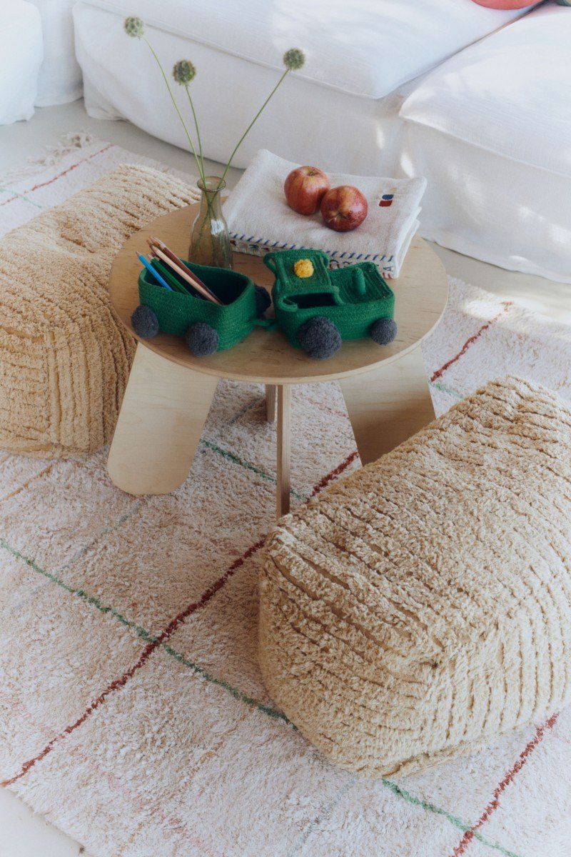 1. Green cotton tractor basket with trailer on wooden table surrounded by beige poufs in a cozy room