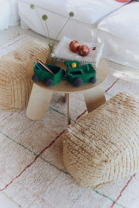 1. Green cotton tractor basket with trailer on wooden table surrounded by beige poufs in a cozy room