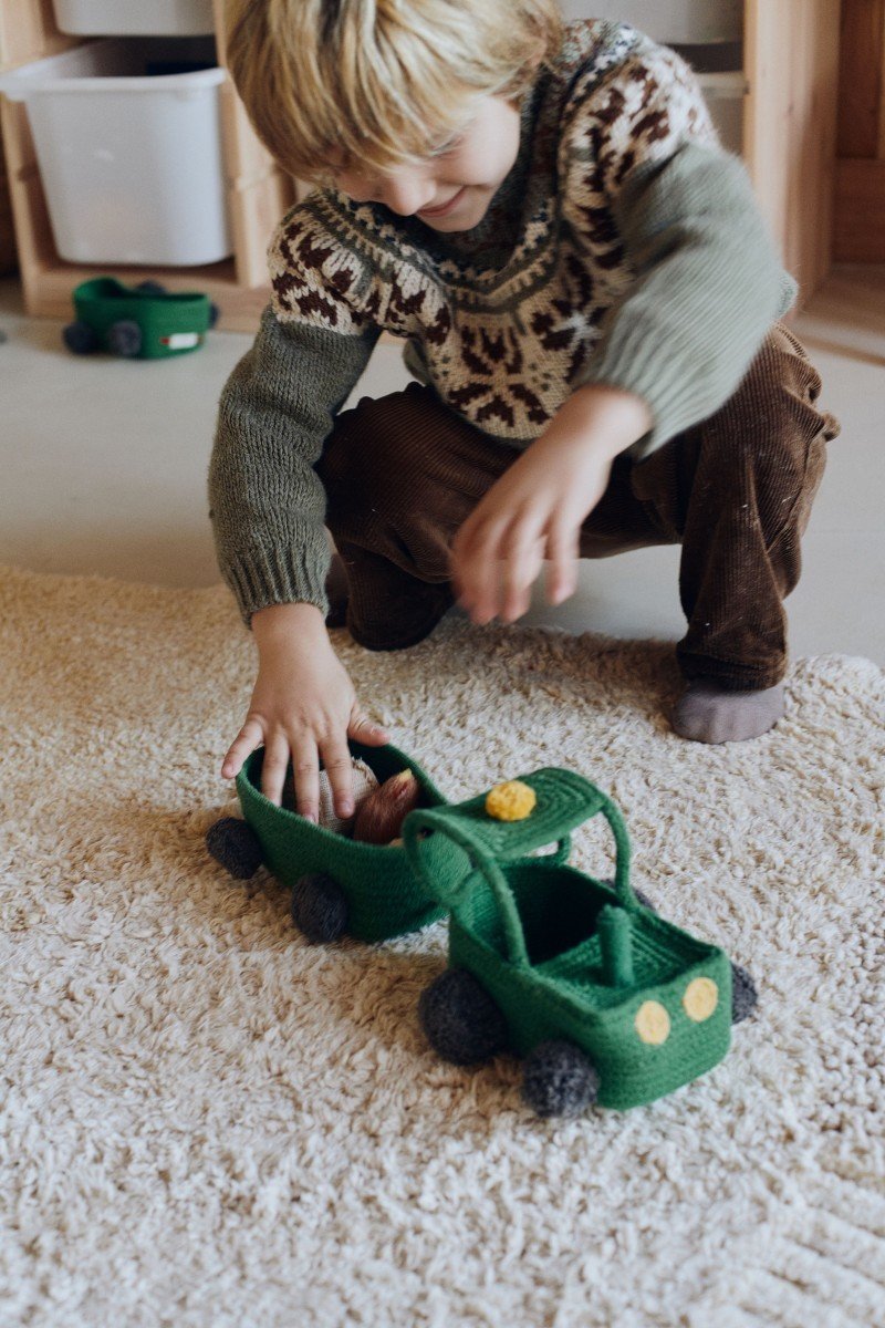 1. Child playing with green cotton decorative basket shaped like a tractor on a beige carpet