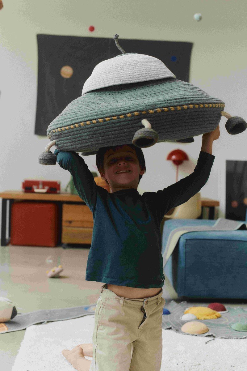 1. Child holding Lorena Canals UFO-shaped decorative basket with movable legs and string antenna in a playroom setting